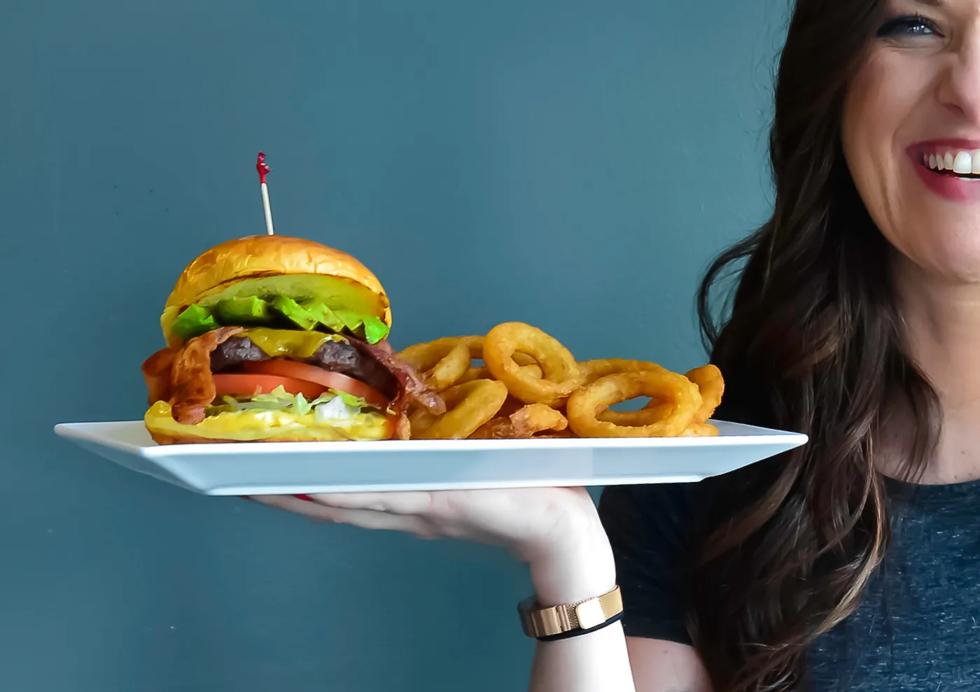 A server holding a stacked burger and onion rings at Bob’s Burgers & Brew