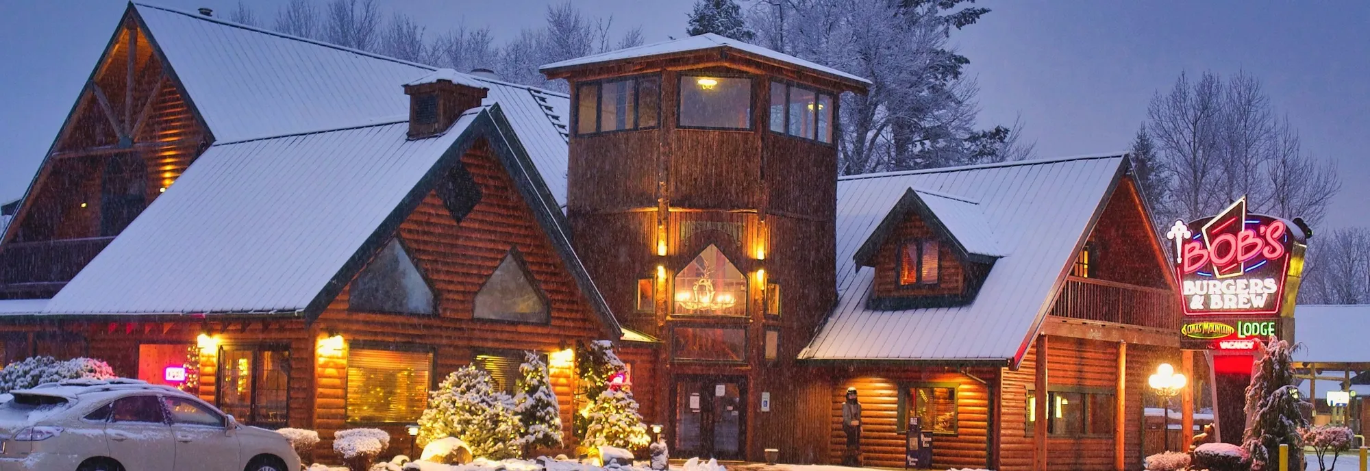 Sumas Mountain Lodge at night under fresh snow, with the Bob’s Burgers & Brew neon sign lit